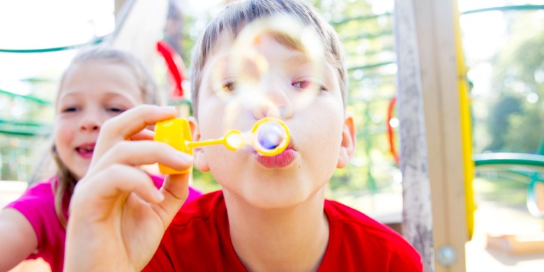 Blond pojke i röd tröja blåser såpbubblor