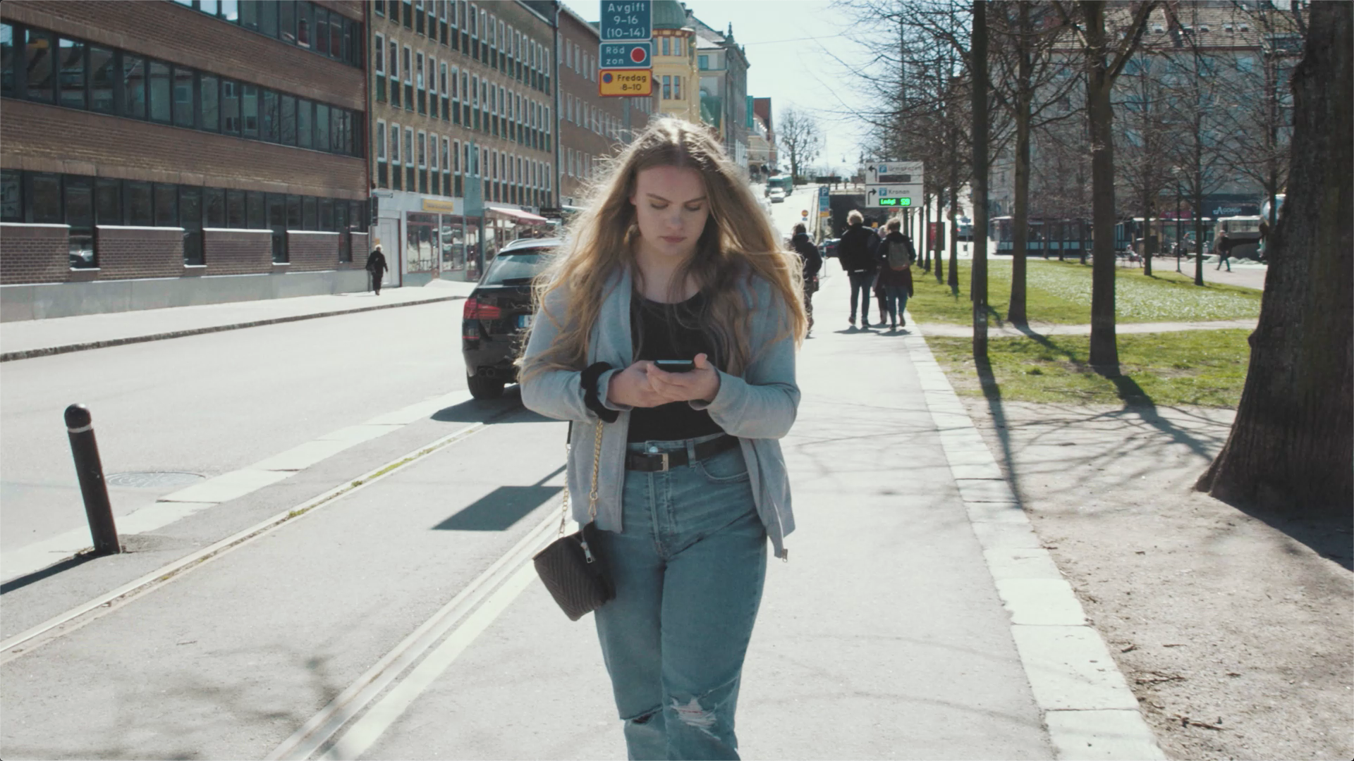 Tjej g&aring;r p&aring; stan och tittar ner i sin mobiltelefon.