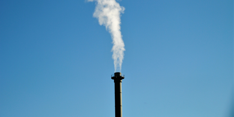 Industriskorsten bolmar ut vit rök mot en blå himmel