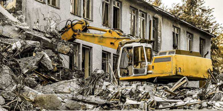 Gul grävmaskin river ett betonghus med sin skopa