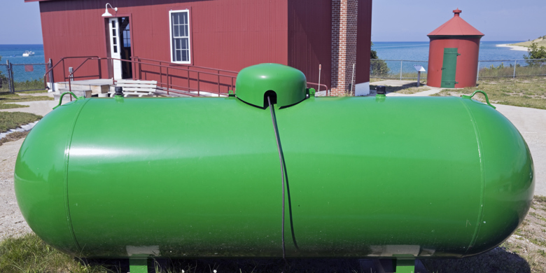 Grön oljecistern, tank, med rött hus och hav i bakgrunden