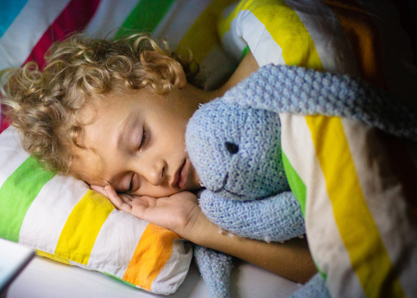 Barn sover i säng med ljusblå kanin som gosedjur