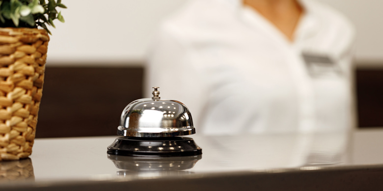 Serviceklocka på hoteldisk framför receptionist.